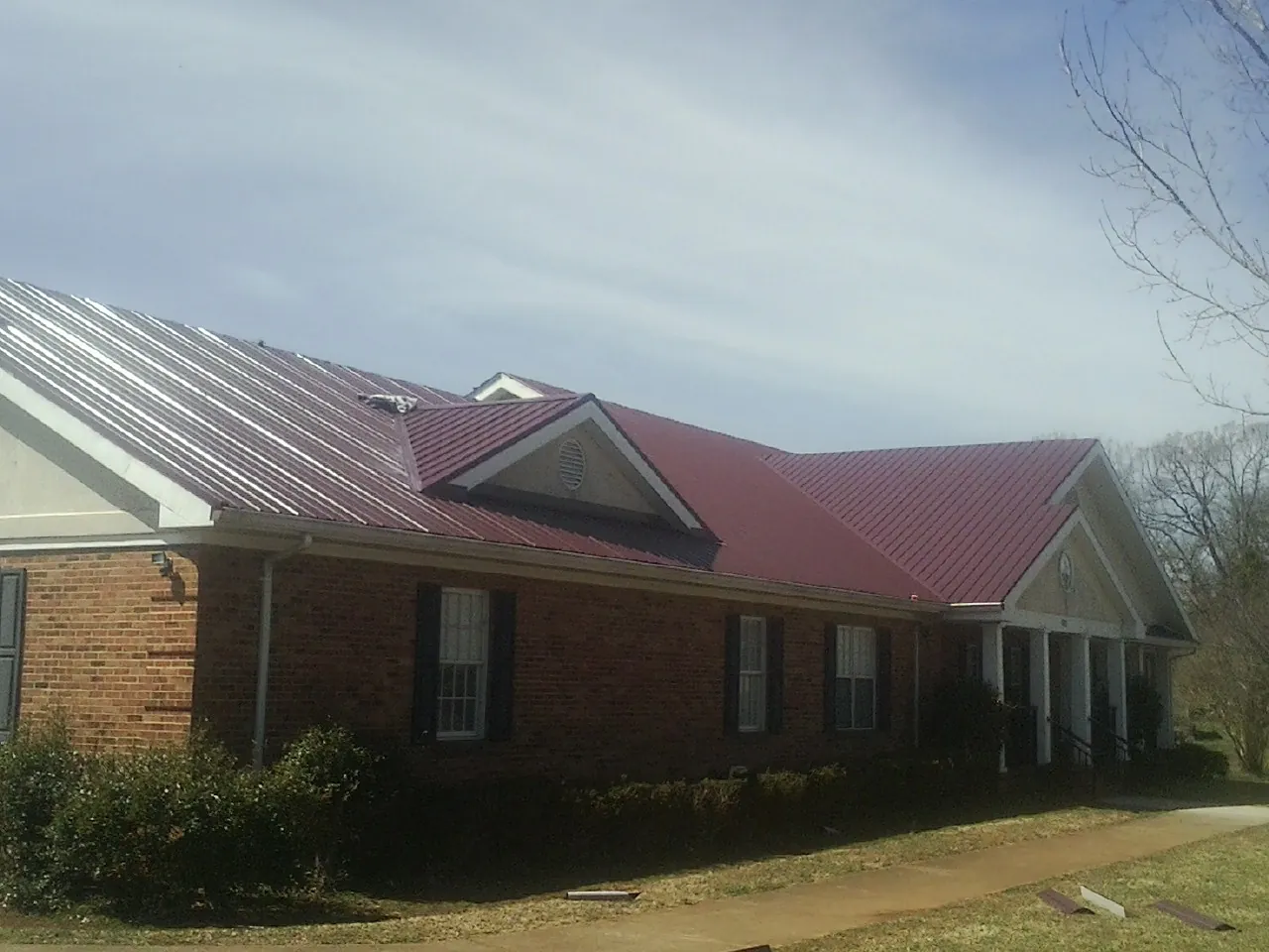 Red metal roof with gabled entries on a long brick building, from a Hail Damage Roof Repair job in Carrollton