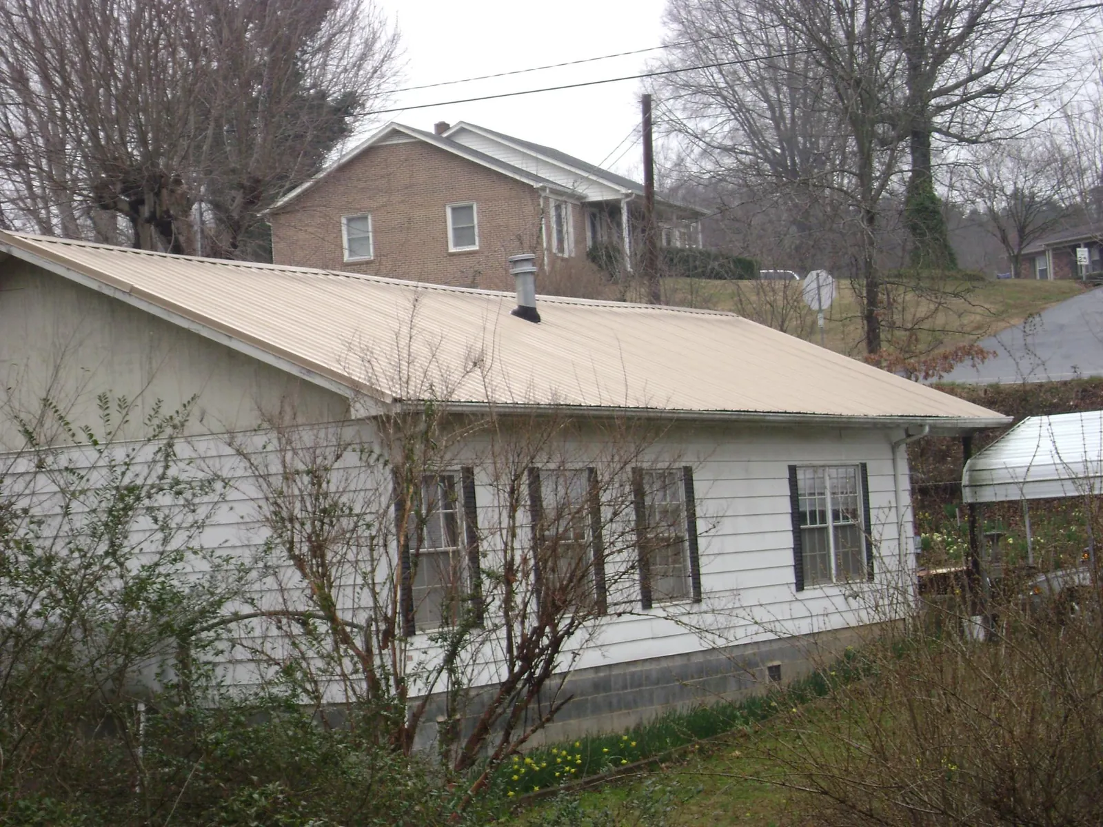 Tan metal roof on a white sided house set into a hillside — Commercial Roofing by Roofing Brothers in Carrollton